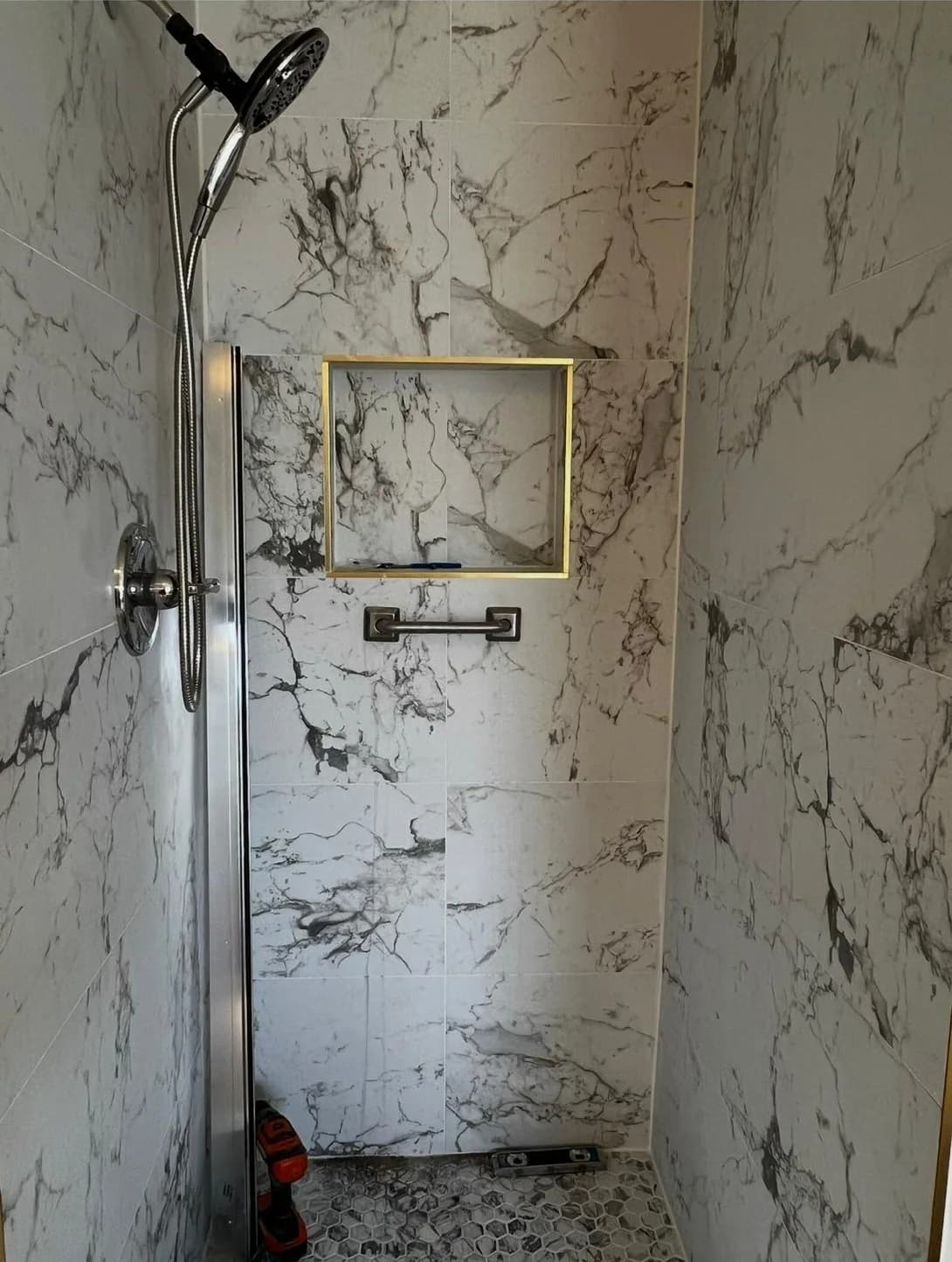 Walk-in shower tiled in veined porcelain with a recessed niche and mosaic floor