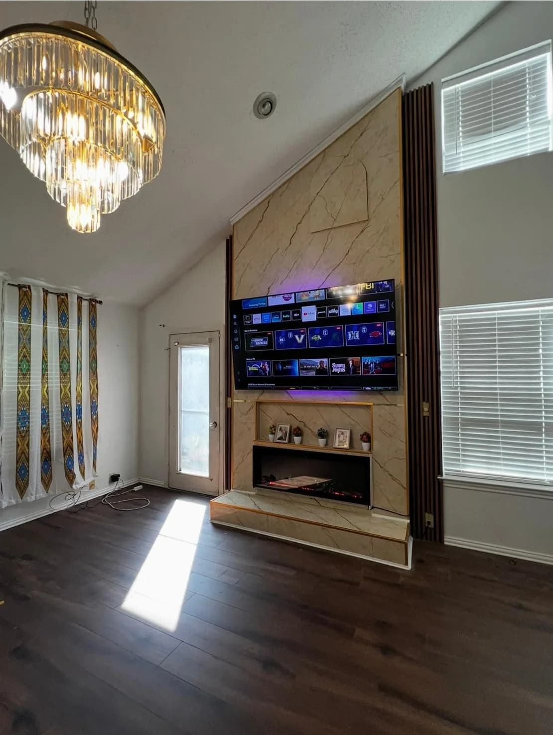 Fireplace wall seen from the room, chandelier and hardwood flooring in frame
