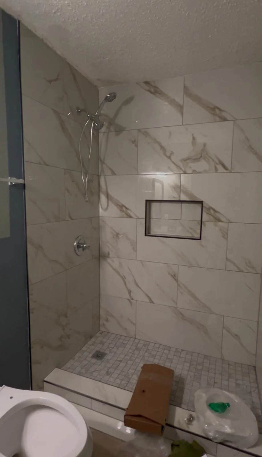 The rebuilt shower tiled floor to ceiling in large-format marble-look porcelain